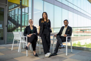 Students posing for a photo. One student in the middle standing flanked by two students sitting